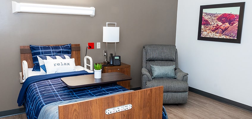 Resident room with a comfortable chair beside the bed.