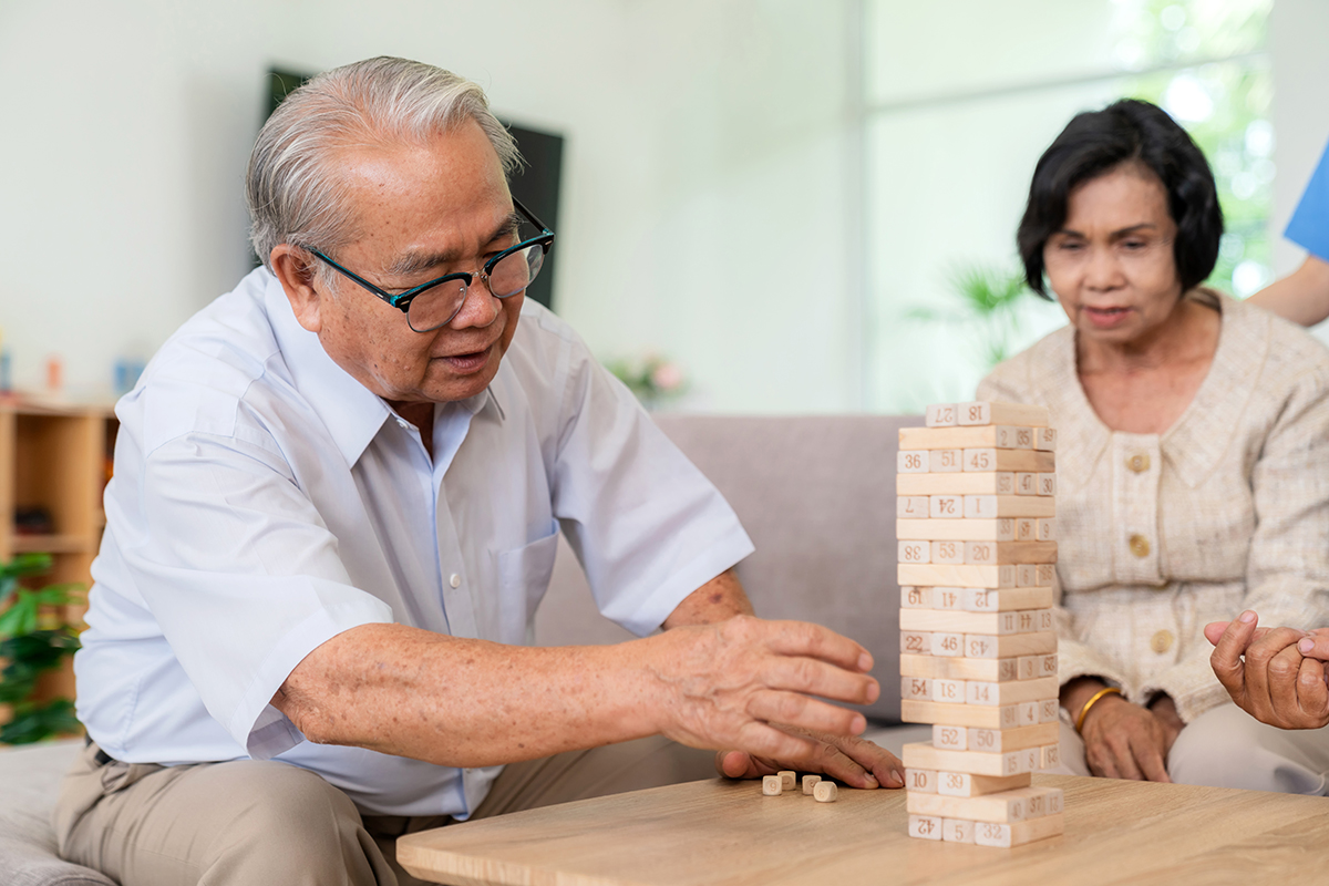 Dementia therapy in playful way. Group of senior elder people stay at nursing home, enjoy activity relation playing Jenga or tumbling tower wood block game. Training fingers and fine skills